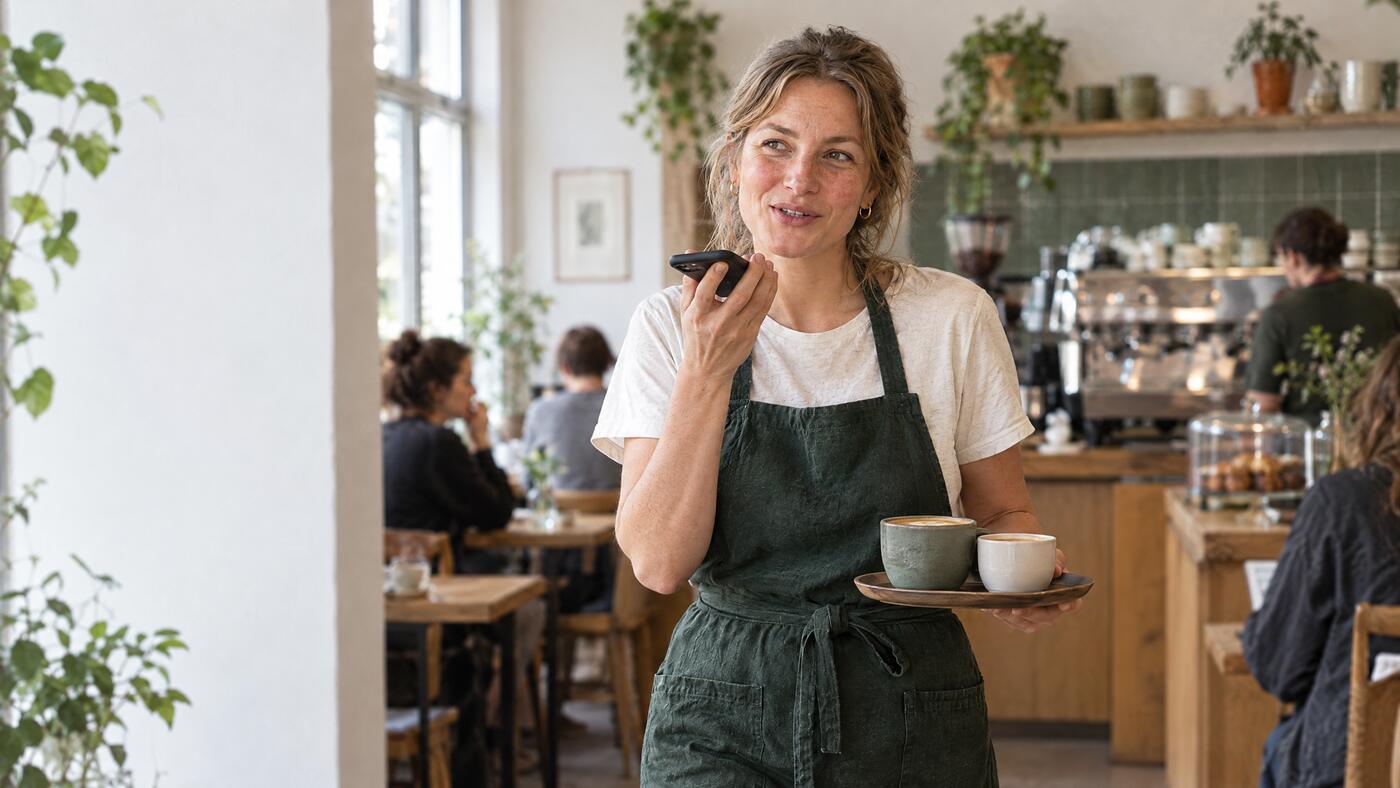 Alex spricht im Café eine Sprachnachricht ins Handy